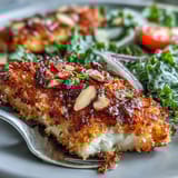 Golden-brown Almond-Crusted Chicken breasts rest beside a vibrant kale salad featuring cherry tomatoes and red onion. 