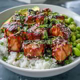 Golden baked salmon cubes rest on fluffy jasmine rice with edamame, cucumber, and avocado slices.