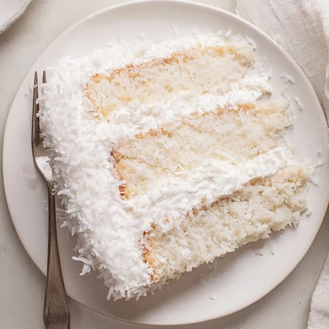 Freshly baked coconut cake layered with sweet coconut filling and billowy meringue frosting on a platter.
