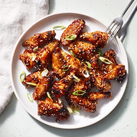 Freshly baked Asian Sticky Wings are arranged on a wire rack, showing their caramelized edges and glistening glaze up close.