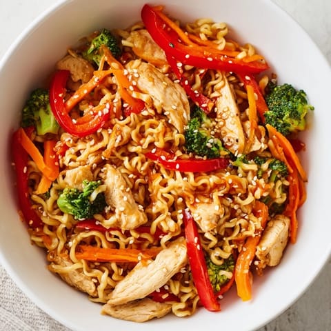 A close-up of Spicy Ramen Stir-Fry in a white bowl, garnished with sesame seeds and fresh cilantro.