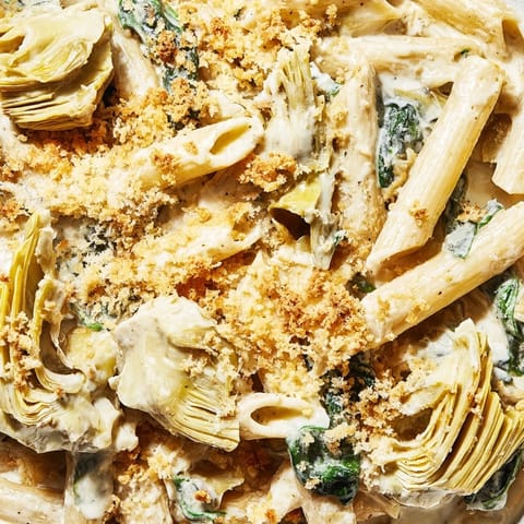 Golden brown Artichoke Pasta Bake bubbling with creamy Parmesan sauce and tender spinach in a rustic baking dish.  