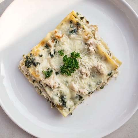 A close-up of sliced Chicken Alfredo Lasagna revealing creamy ricotta, wilted spinach, and perfectly baked pasta layers.  