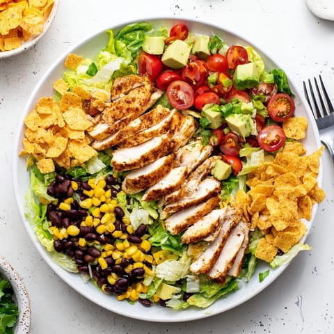 A vibrant bowl of Crunchy Taco Chicken Salad with seasoned chicken, fresh romaine, black beans, and crushed taco shells.