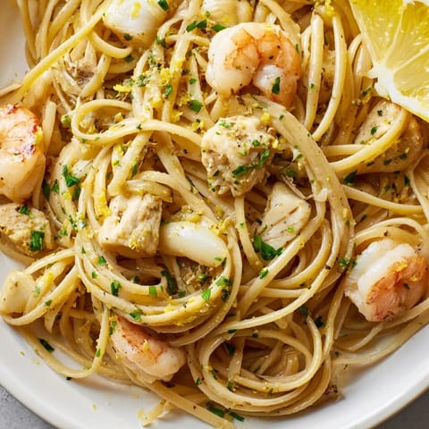 Shrimp and chicken pasta garnished with fresh parsley and lemon wedges on a rustic wooden table.