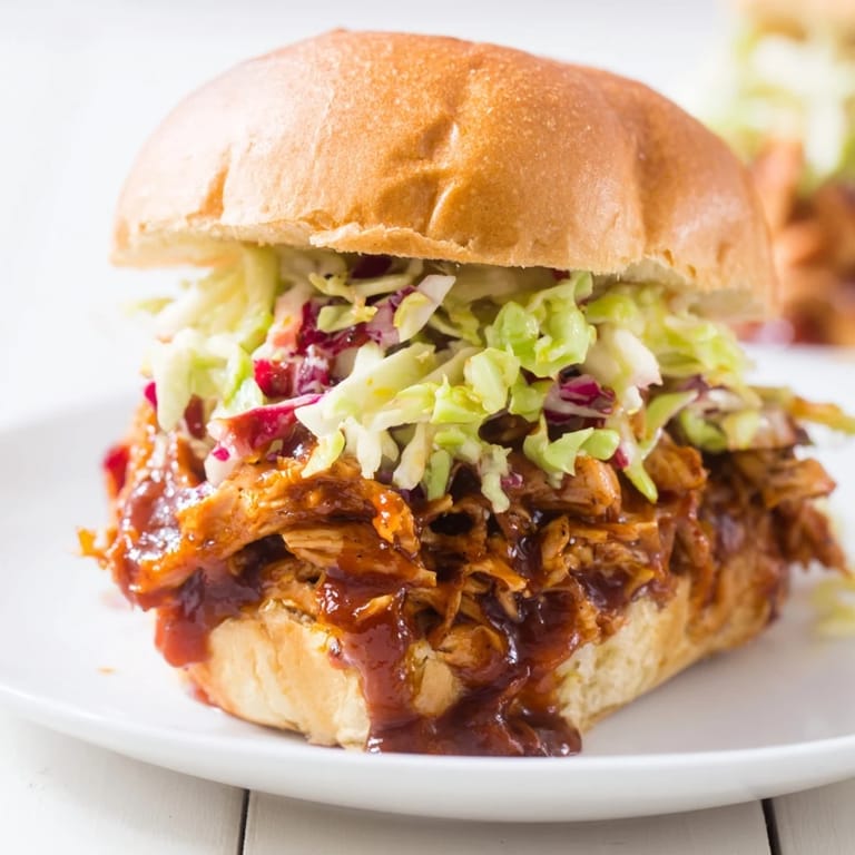 A close-up of pulled BBQ chicken sliders with coleslaw, served on a platter for a party.  