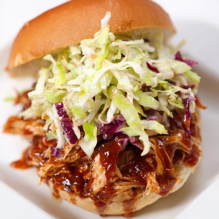 Tender shredded BBQ chicken sliders with tangy slaw on soft mini buns, ready to serve.