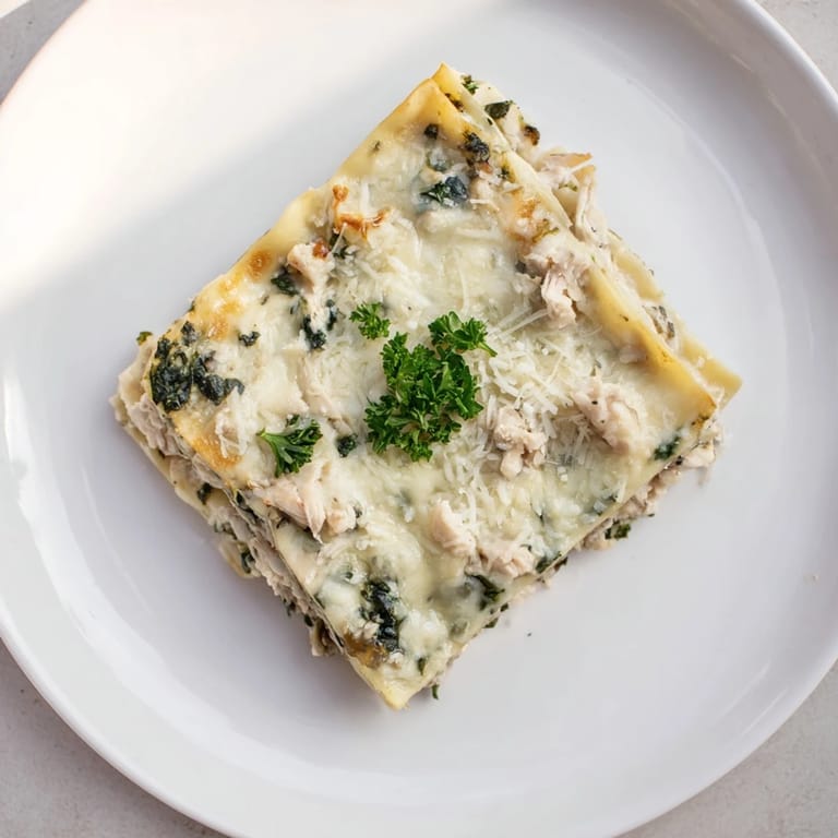 A close-up of sliced Chicken Alfredo Lasagna revealing creamy ricotta, wilted spinach, and perfectly baked pasta layers.  