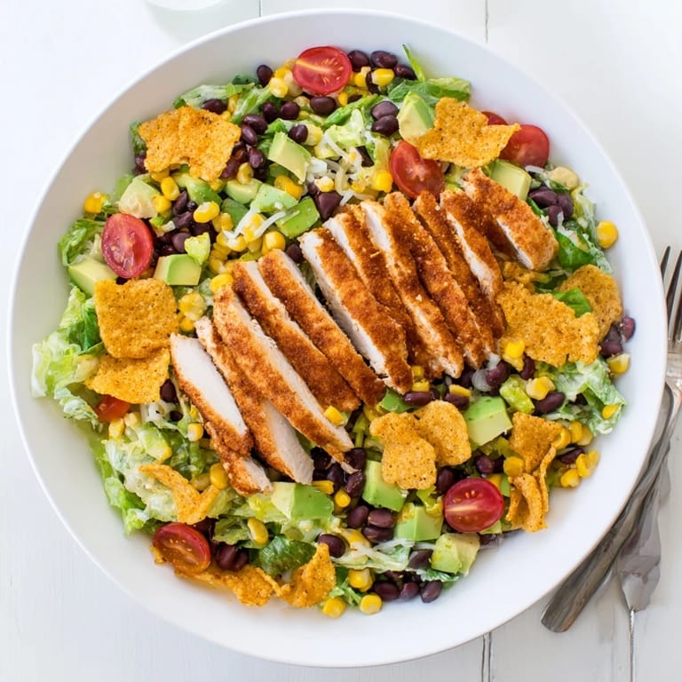 Close-up view of Crunchy Taco Chicken Salad featuring sliced taco-seasoned chicken, corn, tomatoes, and crunchy taco shell pieces.