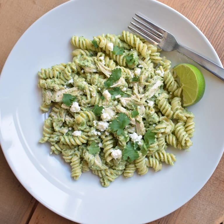Hearty Cilantro Lime Chicken Pasta garnished with crumbled cotija, fresh cilantro, and lime wedges on the side.