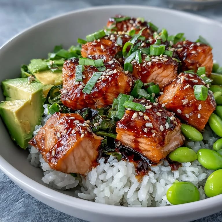 Spicy sriracha mayo drizzles over a fresh Salmon Rice Bowl garnished with sesame seeds and green onions.
