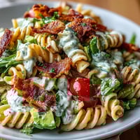 A colorful bowl of BLT pasta with avocado ranch, featuring crispy bacon, juicy tomatoes, and fresh lettuce in a creamy dressing.  